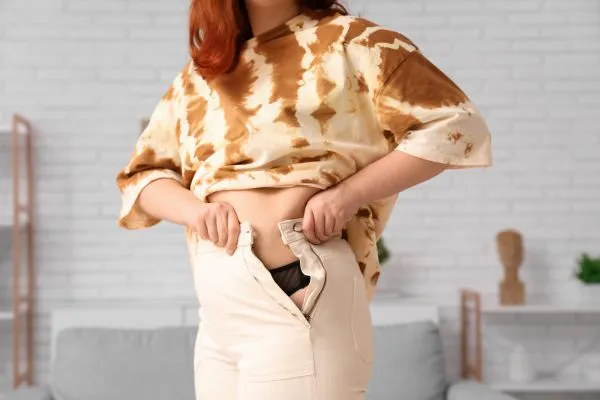 Image of woman trying to do her trousers up after pregnancy weight gain Nottingham